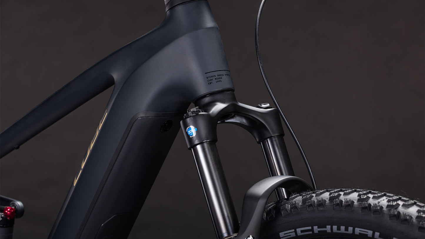 Nahaufnahme des CUBE Stereo Hybrid ONE22 Pro 800 night'n'chrome 2026 Rahmens, die das mattschwarze Finish, die vordere Federgabel, das Reifenprofil mit Schwa-Branding, die Lenkerkabel und die teilweise Integration der CUBE Kinematik vor einem dunklen Hintergrund zeigt.