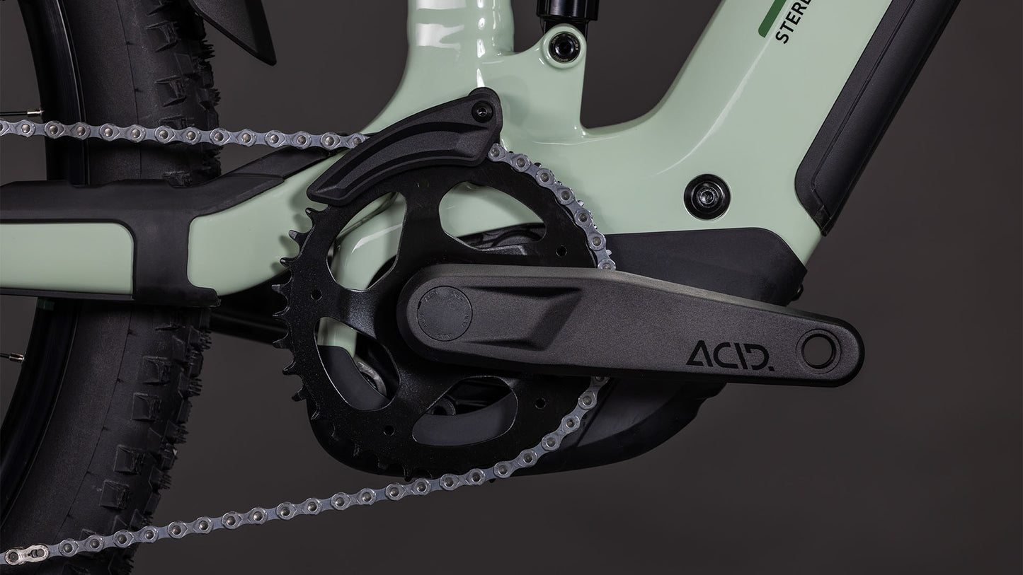 Nahaufnahme der schwarzen Kurbelgarnitur und des Kettenblatts an einem hellgrünen Cube Stereo Hybrid ONE22 Pro 800 stonegrey'n'black 2026, mit CUBE Schriftzug am Kurbelarm, E-Mountainbike-Reifen, Antrieb und Bosch CX Antriebssystem.