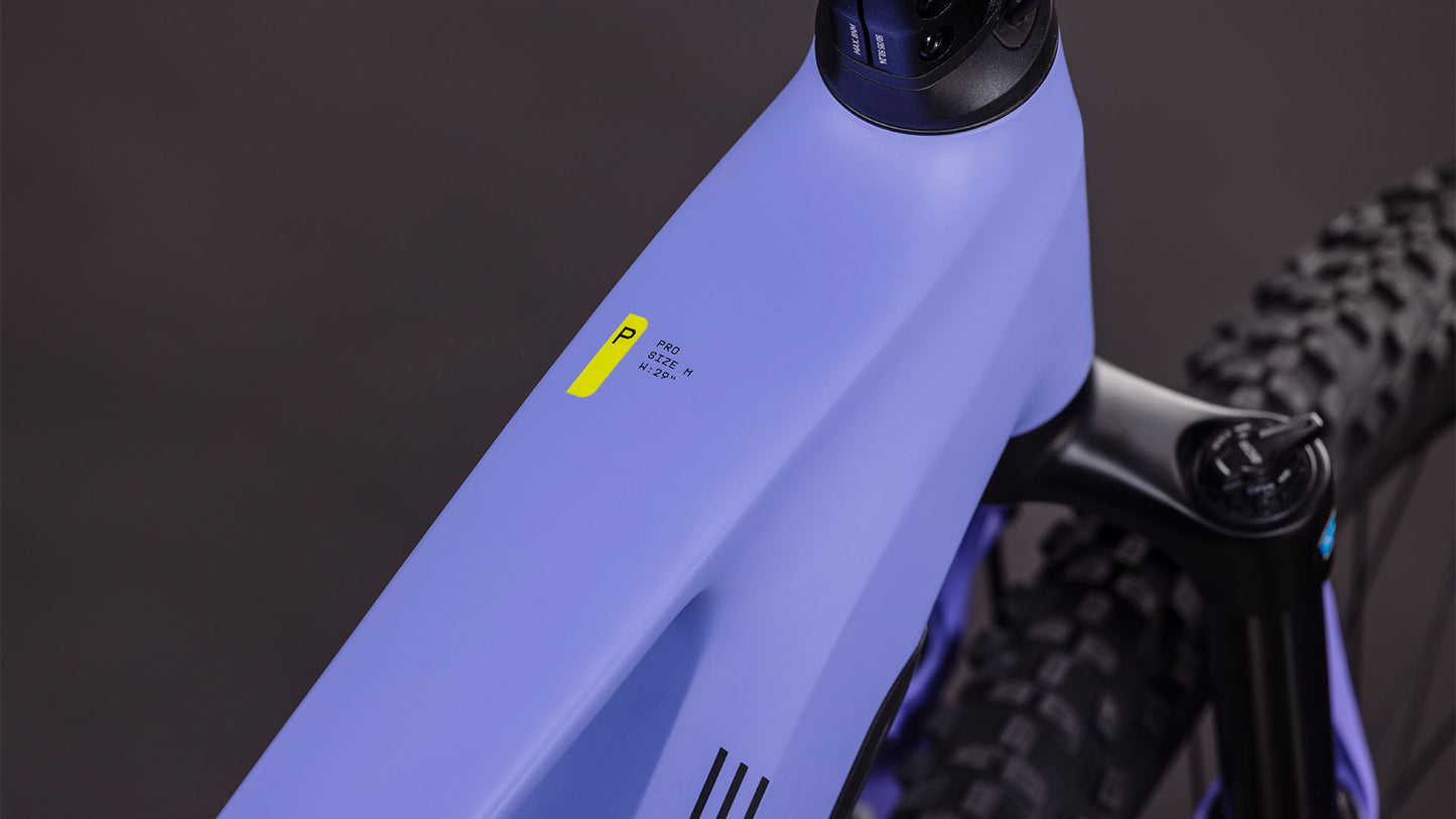 Nahaufnahme des mattvioletten CUBE Stereo Hybrid ONE22 Pro 800 lucidlilac'n'lime 2026 E-MTB-Rahmens mit gelbem und schwarzem Etikett, einem Teil der Federgabel und dem Bosch CX-Antrieb vor einem verschwommenen dunklen Hintergrund.