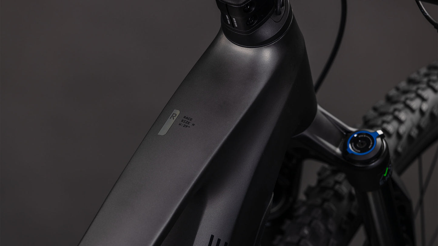 Nahaufnahme des mattschwarzen CUBE Stereo Hybrid ONE22 Race 800 slabgrey'n'chrome 2026 Rahmens, der das Oberrohr, die Vorderradaufhängung, die Shimano 12-fach XT Schaltung und das Reifenprofil vor einem dunklen Hintergrund hervorhebt.