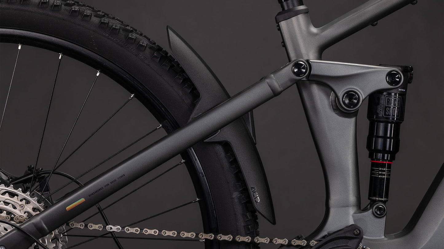 Nahaufnahme der Hinterradfederung und des Shimano XT-Antriebs des CUBE Stereo Hybrid ONE22 Race 800 slabgrey'n'chrome 2026 mit Hinterrad, Stoßdämpfer, Kette und mattschwarzem Schutzblech vor dunklem Hintergrund.