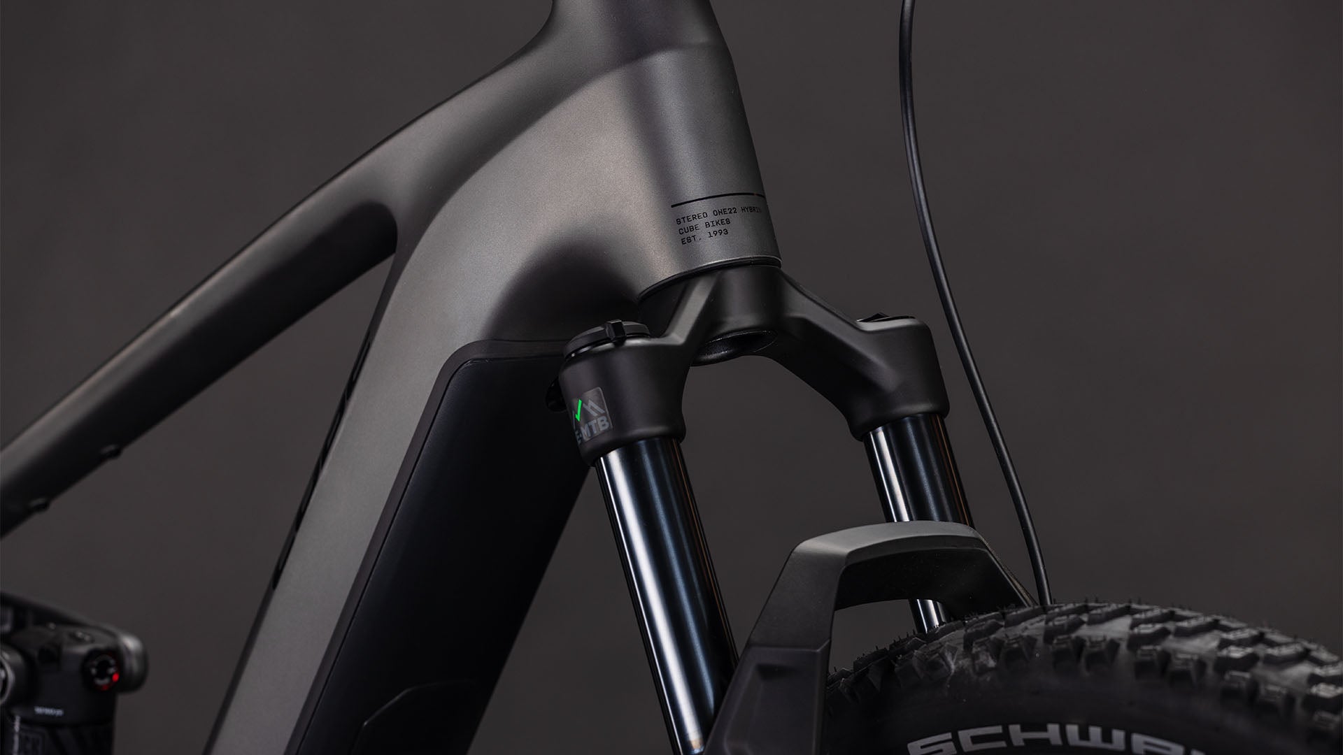 Nahaufnahme des mattschwarzen CUBE Stereo Hybrid ONE22 Race 800 slabgrey'n'chrome 2026-Rahmens und der Federgabel, mit Noppenreifen und Schwalbe-Branding sowie Shimano 12-fach XT-Schaltungsdetails vor dunklem Hintergrund.