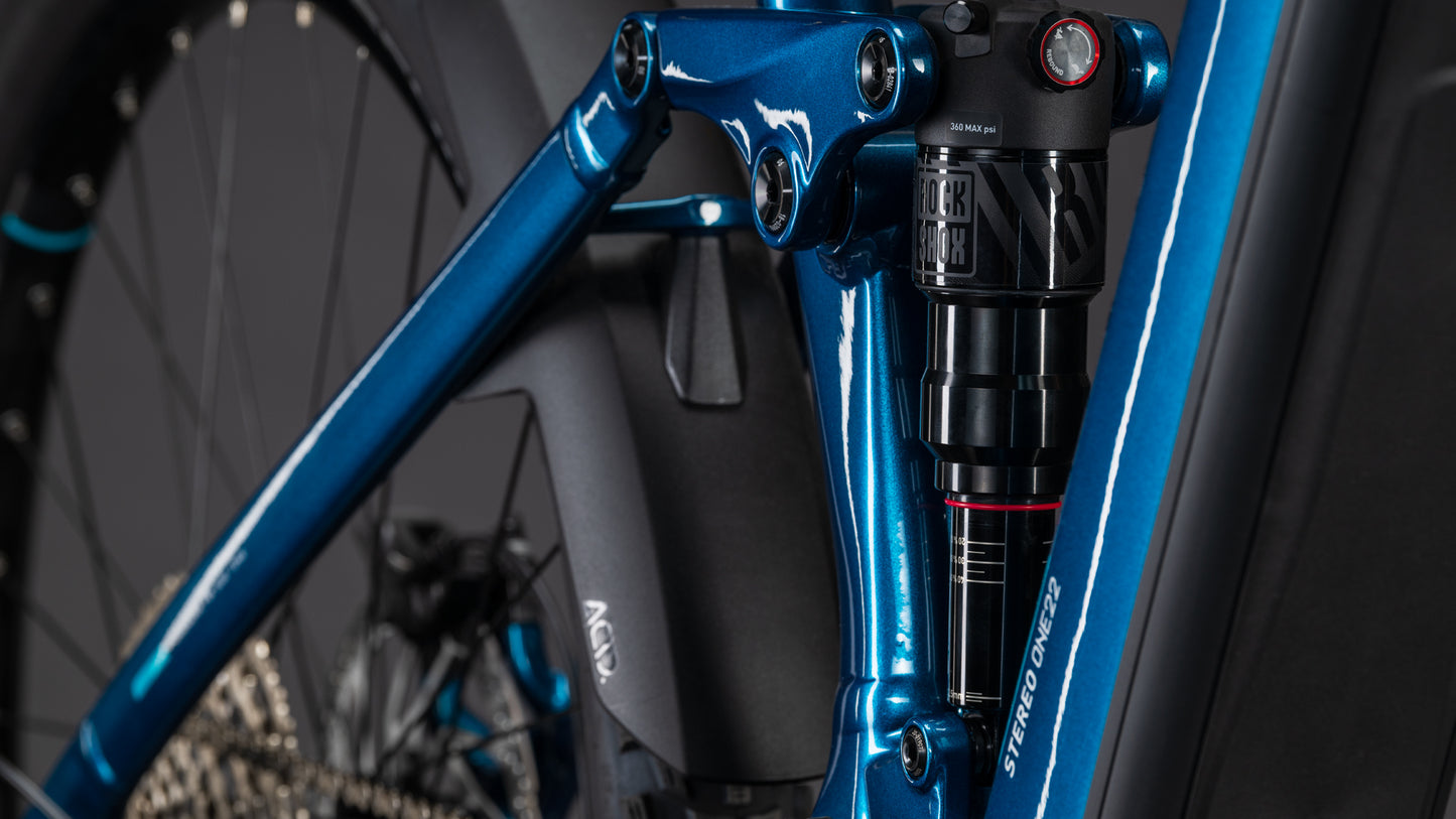Nahaufnahme des CUBE Stereo Hybrid ONE22 Race 800 electricblue'n'white 2026 Rahmens, mit Hervorhebung der hinteren Federung und des Gestänges, wobei das Hinterrad, die Schaltung und die Shimano 12-fach XT-Kettenschaltung sichtbar sind.