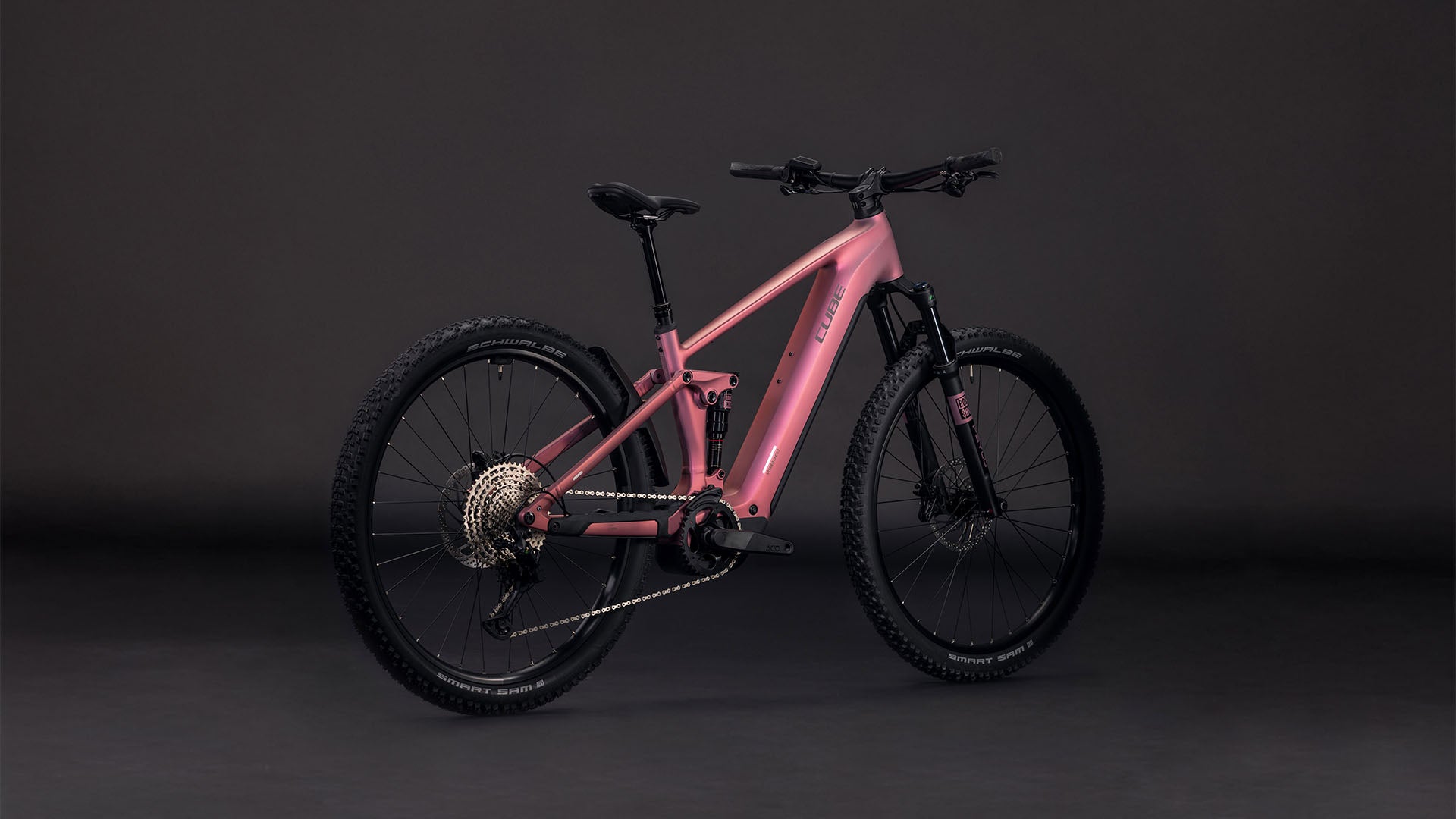 Das CUBE Stereo Hybrid ONE22 Race 800 shiftblush'n'black 2026 Mountainbike, ausgestattet mit dicken Stollenreifen, Bosch CX Motor, fortschrittlicher Federung und einem eleganten rosa-schwarzen Rahmen, wird vor einem dunklen Hintergrund präsentiert.