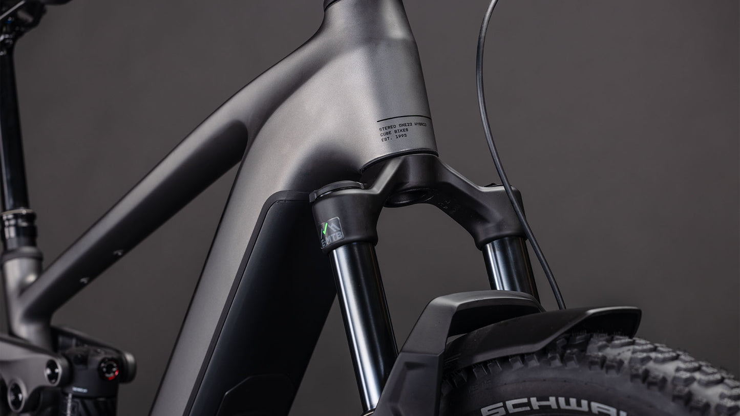 Nahaufnahme des mattschwarzen Vorderrahmens und der Federgabel des CUBE Stereo Hybrid ONE22 Race 800 FE slabgrey'n'chrome 2026 mit den dicken Schwalbe-Reifen und dem integrierten Bosch CX Motor. Der dunkle Hintergrund unterstreicht sein modernes Design.