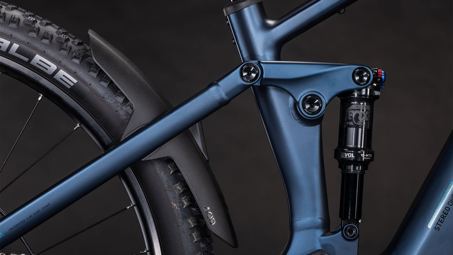 Nahaufnahme des CUBE Stereo Hybrid ONE22 SLX 800 indigoblue'n'blue 2026 Rahmens, mit Hervorhebung der hinteren Federung, des Stoßdämpfers, des SCHWALBE Hinterreifens und der Bosch CX Antrieb Details vor einem dunklen Hintergrund.