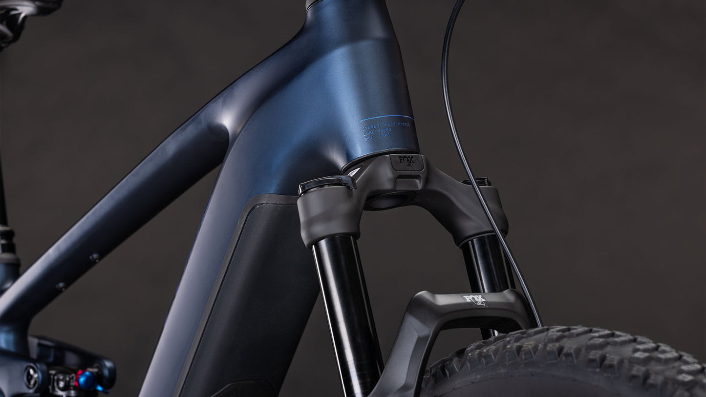 Nahaufnahme des mattblauen Rahmens und der Federgabel des CUBE Stereo Hybrid ONE22 SLX 800 indigoblue'n'blue 2026 mit Bosch CX-Motor und Shimano XT 12-Gang-Schaltung, dargestellt mit einem schwarzen Reifen vor dunklem Hintergrund.