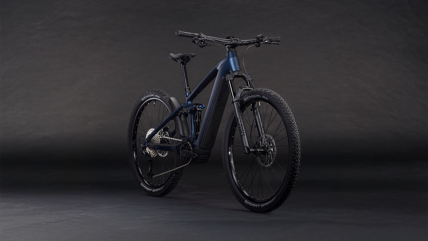 Das CUBE Stereo Hybrid ONE22 SLX 800 indigoblue'n'blue 2026, ein schnittiges E-MTB mit robuster Bereifung und Bosch CX-Antrieb, wird auf einem dunklen, nahtlosen Hintergrund gezeigt, der sein Front- und Seitenprofil hervorhebt.