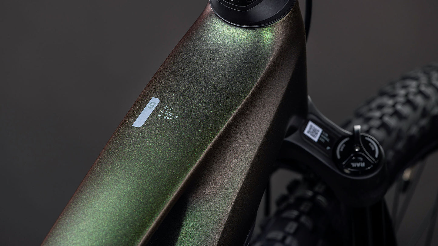 Nahaufnahme des metallisch glänzenden, dunkelgrünen Rahmens des CUBE Stereo Hybrid ONE22 SLX 800 stellar'n'green 2026 E-Fully, die ein kleines Etikett und einen Teil des Lenkers vor einem dunklen, verschwommenen Hintergrund zeigt.