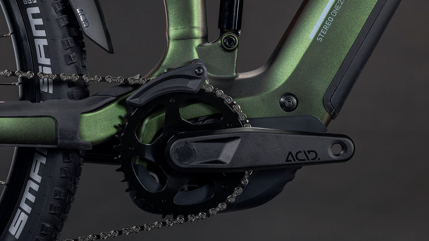 Nahaufnahme des ACID-Kurbelarms, des Kettenblatts und des Hinterradreifens am CUBE Stereo Hybrid ONE22 SLX 800 stellar'n'green 2026 e-mtb mit Bosch CX Antrieb und grünem Rahmen vor dunklem Hintergrund.