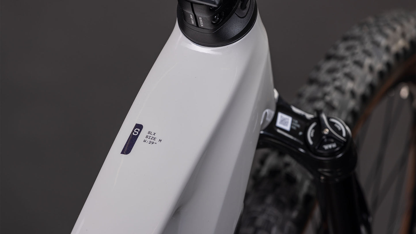 Nahaufnahme eines CUBE Stereo Hybrid ONE22 SLX 800 greige'n'switch 2026 Rahmens mit "SLX SIZE M M/17-18" Aufkleber, Federgabel, Knobby Reifen und Bosch CX Antrieb im Hintergrund.