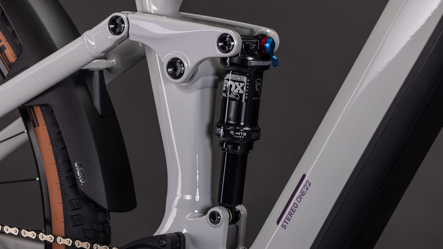 Nahaufnahme der Hinterradaufhängung und des Stoßdämpfers an einem CUBE Stereo Hybrid ONE22 SLX 800 greige'n'switch 2026, mit einem Teil des Hinterreifens - ideal für Fahrer, die die Vorteile von E-Fully und Bosch CX Antrieb nutzen möchten.