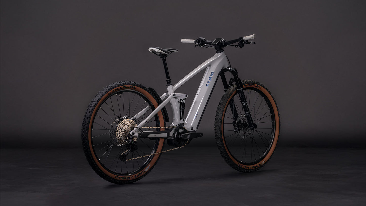 Das CUBE Stereo Hybrid ONE22 SLX 800 greige'n'switch 2026 ist ein modernes E-Fully-Mountainbike mit grauem Rahmen, schwarzer und brauner Bereifung, Vorderradfederung und Bosch CX-Antrieb, das im Studio vor dunklem Hintergrund gezeigt wird.