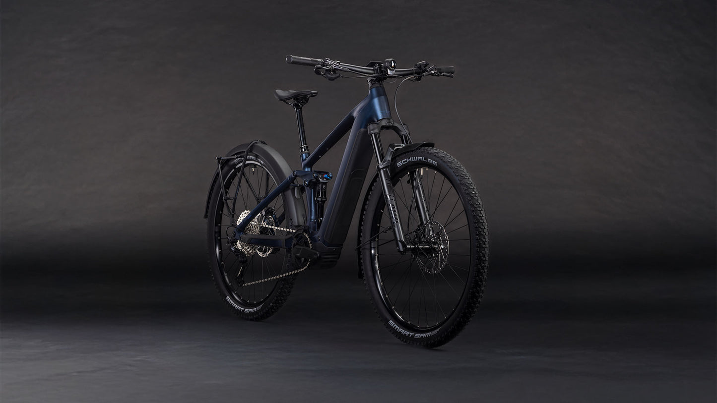 Das CUBE Stereo Hybrid ONE22 SLX 800 FE indigoblue'n'blue 2026 E-Mountainbike mit Bosch CX Motor, breiten Reifen, Schutzblech und Scheibenbremsen ist auf einem dunklen Hintergrund mit Farbverlauf leicht nach links ausgerichtet.