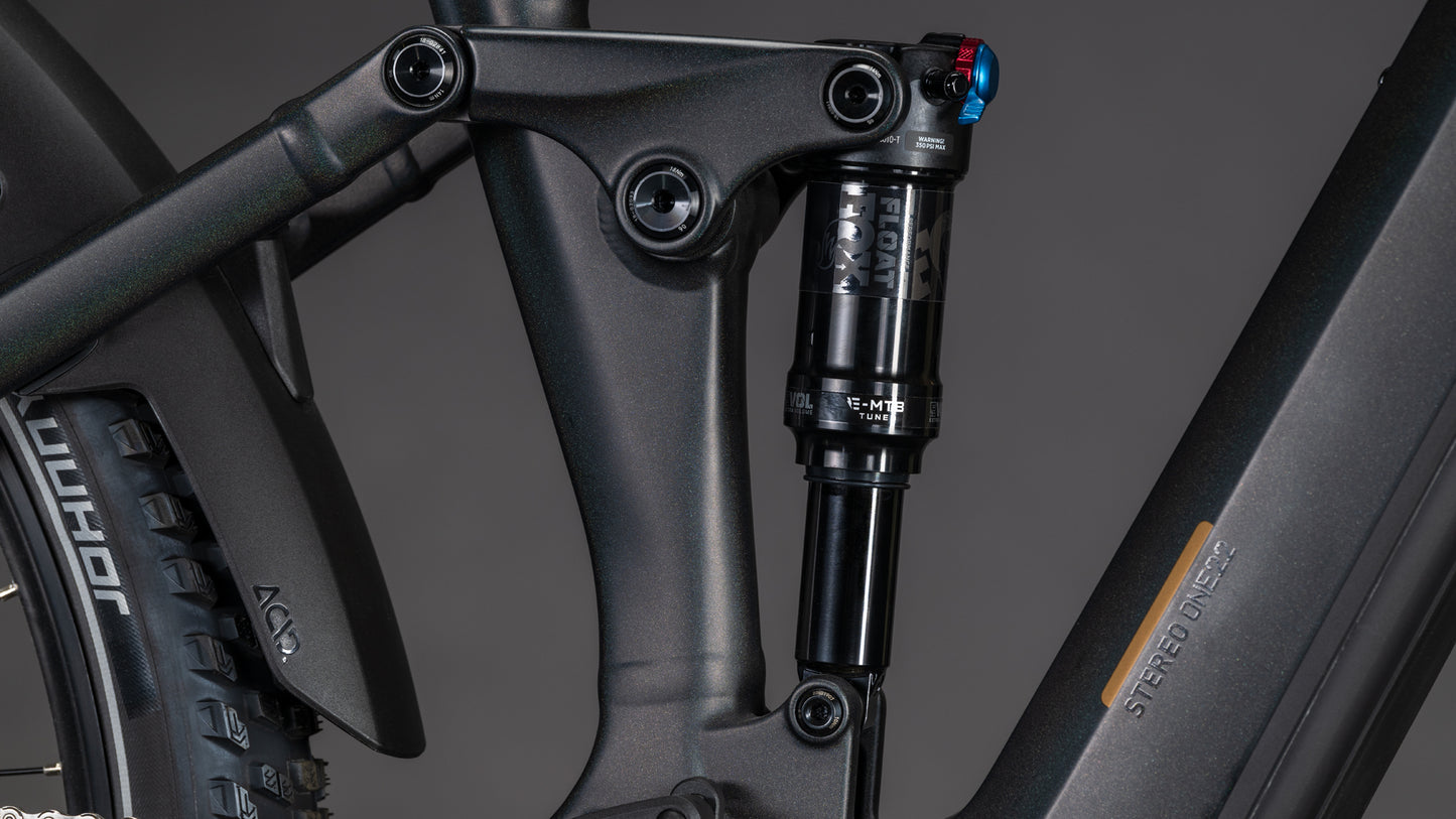 Nahaufnahme eines schwarzen CUBE Stereo Hybrid ONE22 SLT 800 prizmblack'n'black 2026 vollgefederten E-Mountainbike-Rahmens. Hervorzuheben sind der hintere Stoßdämpfer, das Gestänge, das sichtbare Reifenprofil und die Shimano XT Di2 Komponenten.