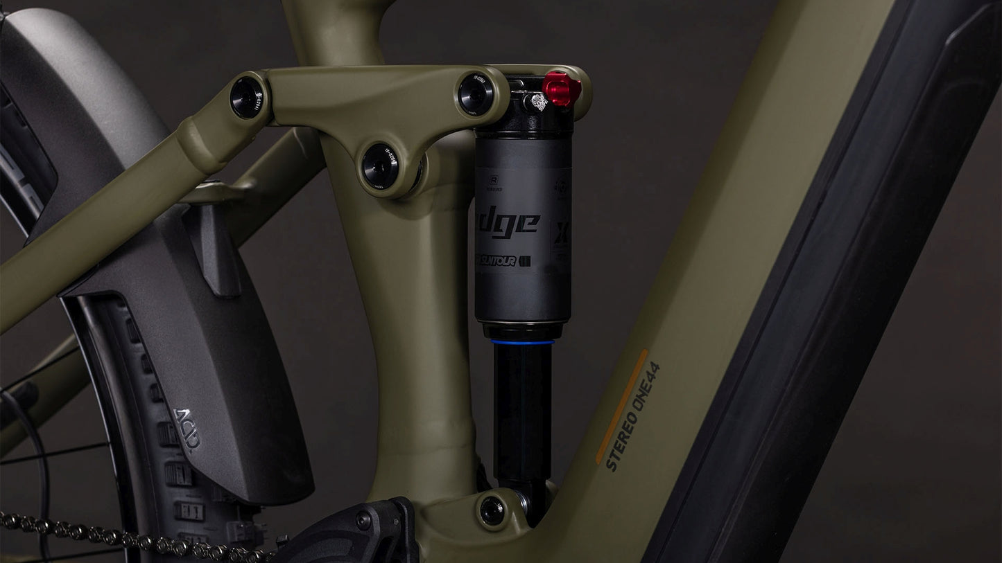 Nahaufnahme der Hinterradaufhängung und des Rahmens des CUBE Stereo Hybrid ONE44 Pro 800 dustyolive'n'gold 2026 mit Shimano XT-Schaltung, Stoßdämpfer und Edge-Label - ein Beweis für die fortschrittliche Technik von CUBE.