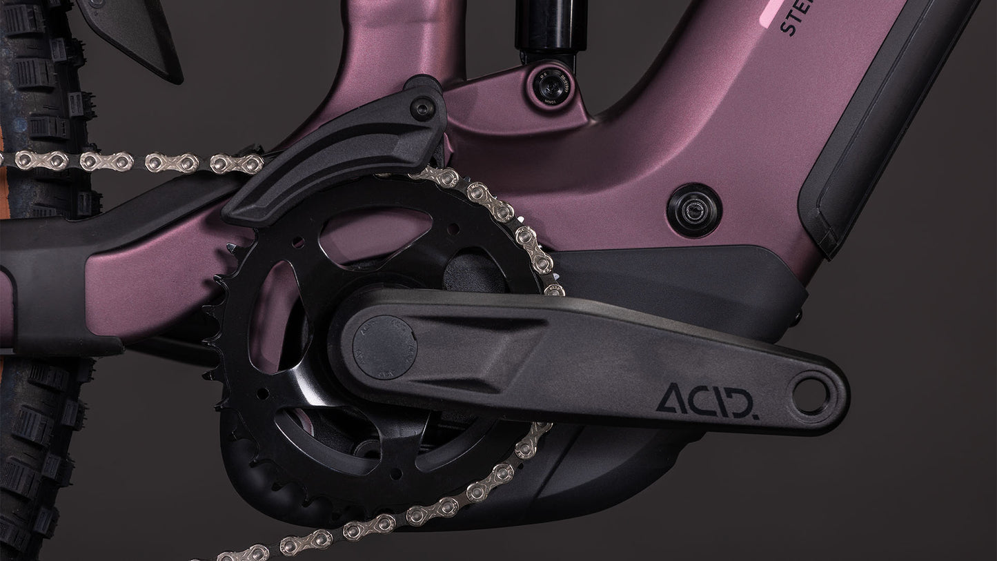 Nahaufnahme der Kurbelgarnitur und des Kettenblatts an einem mattlila CUBE Stereo Hybrid ONE44 Pro 800 Rahmen, Pedalarm mit der Aufschrift ACID, mit detaillierten Kettengliedern und einem dunklen Hintergrund, der die Shimano XT Schaltung hervorhebt.
