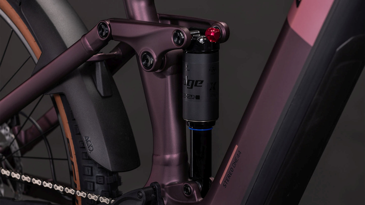 Nahaufnahme eines CUBE Stereo Hybrid ONE44 Pro 800 shiftblush'n'raisin 2026 mit schwarzem Stoßdämpfer am mattlila Rahmen mit Bosch CX Motor sowie Hinterrad, Kette und Schutzblech.