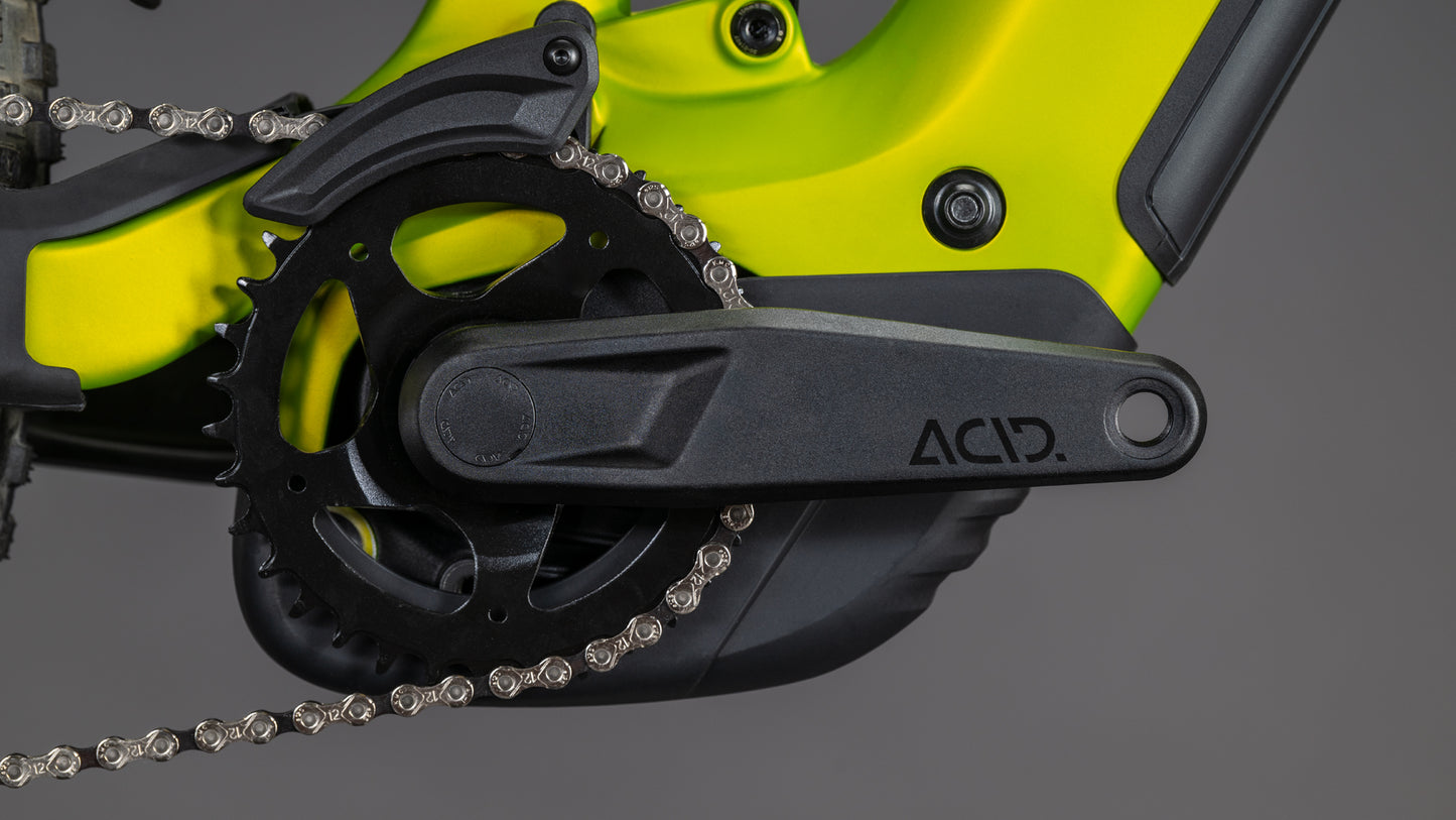 Nahaufnahme der schwarzen ACID-Kurbelgarnitur und des Kettenblatts am CUBE Stereo Hybrid ONE44 Pro 800 lizard'n'black 2026, wobei ein Teil der Kette und der detaillierten Shimano XT-Schaltung vor einem grauen Hintergrund zu sehen ist.
