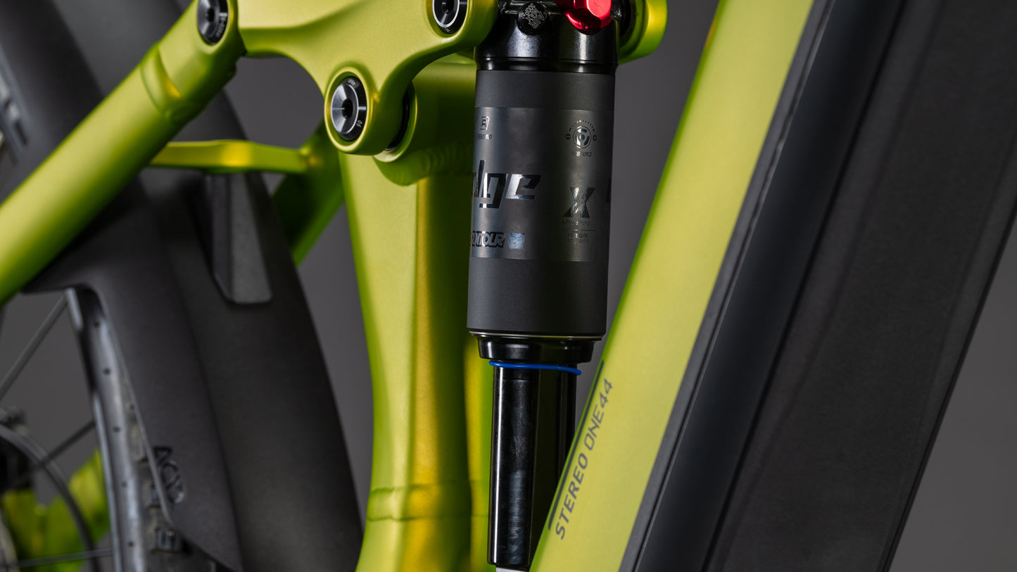 Nahaufnahme der Hinterradaufhängung eines CUBE Stereo Hybrid ONE44 Pro 800 lizard'n'black 2026: schwarzer Stoßdämpfer auf grünem Rahmen mit Aufdruck "STEREO ONE77", der die wichtigsten Designelemente aufgreift.