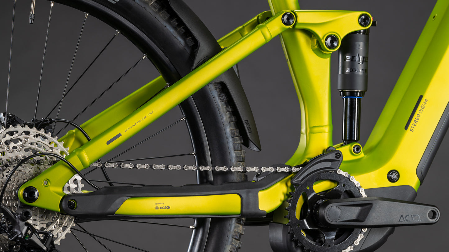 Nahaufnahme der Hinterradaufhängung des CUBE Stereo Hybrid ONE44 Pro 800 lizard'n'black 2026, der Shimano XT Schaltung, der Zahnradkassette, des Bosch CX Motors, der Pedale und des hinteren Stoßdämpfers vor einem schlichten dunklen Hintergrund.