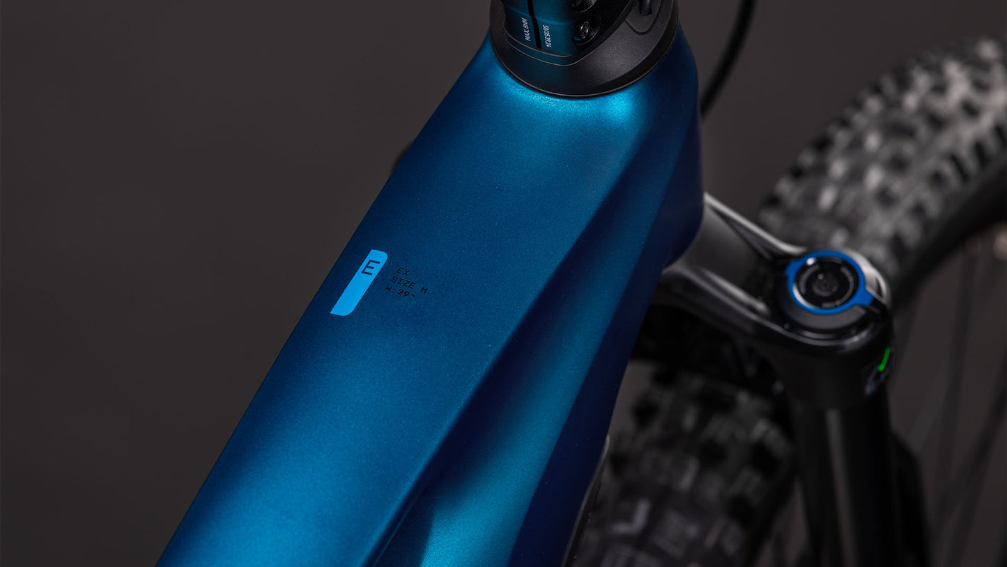 Nahaufnahme des Oberrohrs und der Vorderrad-Federgabel eines CUBE Stereo Hybrid ONE44 EX 800 electricblue'n'blue 2026, mit einem kleinen E-Etikett und einem Teil des strukturierten Reifens, vor einem dunklen Hintergrund.