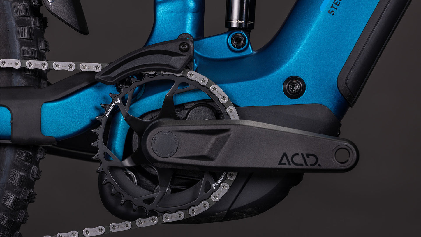 Nahaufnahme der CUBE Stereo Hybrid ONE44 EX 800 electricblue'n'blue 2026 Kurbelgarnitur und des Kettenblatts mit Bosch CX Antrieb, Kette, ACID Pedalarm und einem blauen E-MTB Rahmen vor dunklem Hintergrund.