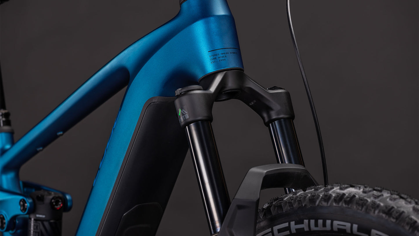 Nahaufnahme der CUBE Stereo Hybrid ONE44 EX 800 electricblue'n'blue 2026 Federgabel und des Rahmens mit dicken Reifen, Schaltzügen und leistungsstarkem Bosch CX-Antrieb vor einem dunklen Hintergrund.