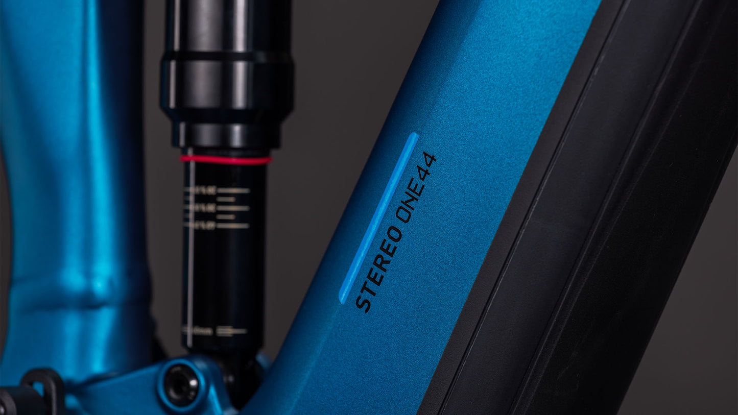 Nahaufnahme des CUBE Stereo Hybrid ONE44 EX 800 electricblue'n'blue 2026-Rahmens mit dem STEREO ONE44-Schriftzug, einem Teil des Aufhängungssystems, und mattschwarzen Akzenten vor dunklem Hintergrund.
