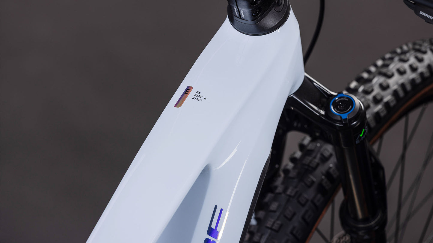 Nahaufnahme eines CUBE Stereo Hybrid ONE44 EX 800 iceblue'n'prism 2026 Rahmens mit Bosch CX Antrieb Display, das Zahlen und Symbole sowie einen Teil des Vorderrads und der Federgabel vor einem dunklen Hintergrund zeigt.