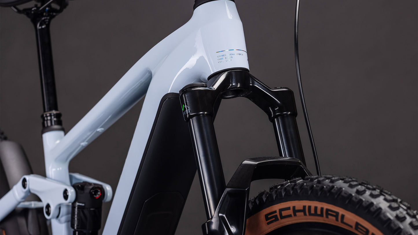 Nahaufnahme der CUBE Stereo Hybrid ONE44 EX 800 iceblue'n'prism 2026 Federgabel und des Schwalbe-Laufrads vor einem dunklen Hintergrund, der die leistungsstarke Bosch CX-Antriebsleistung zeigt.