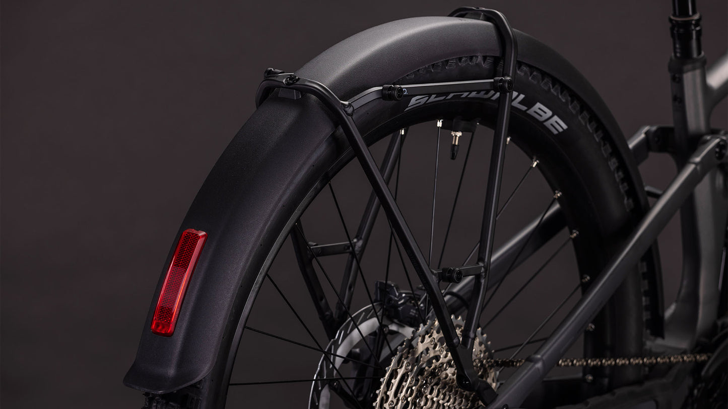 Nahaufnahme des Hinterrads des CUBE Stereo Hybrid ONE44 EXC 800 FE irongrey'n'chrome 2026, wobei ein schwarzes Schutzblech mit rotem Reflektor, eine Shimano XT-Kassette und ein Schwalbe-Reifen vor einem dunklen Hintergrund hervorgehoben werden.