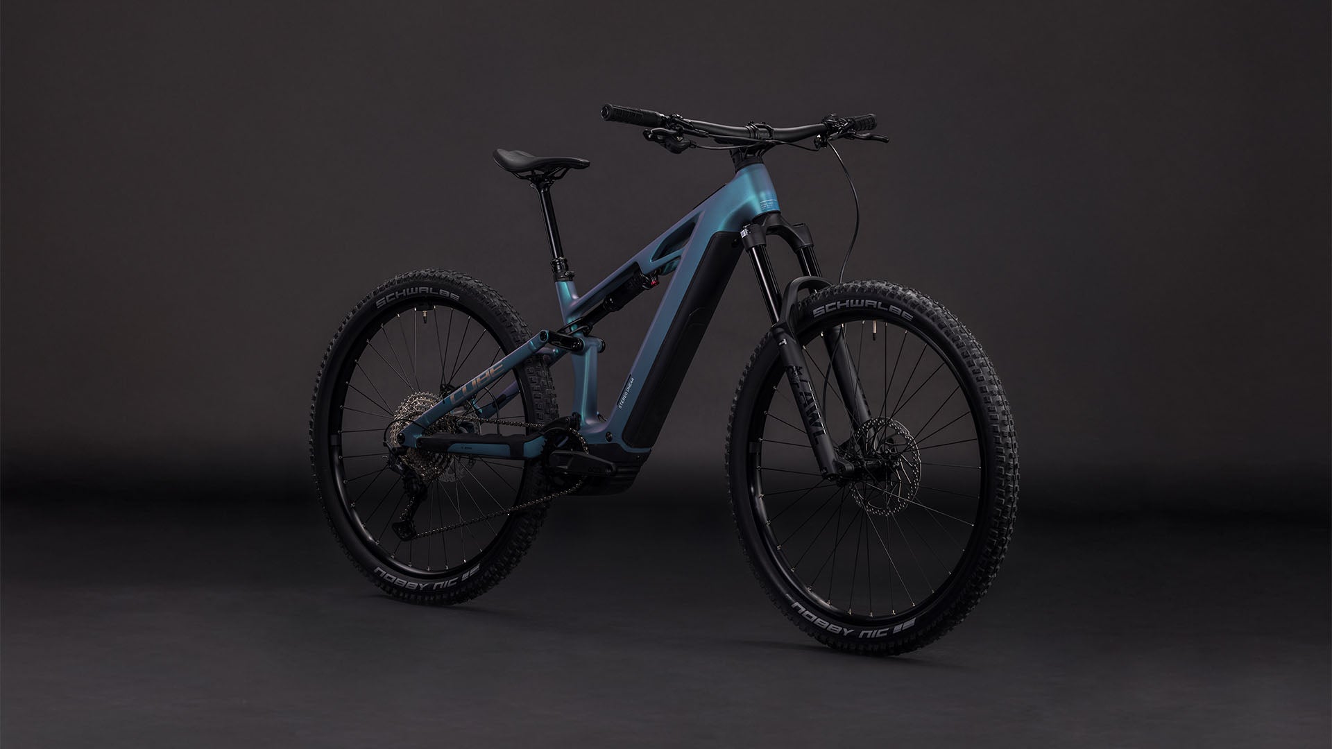 Das vollgefederte Mountainbike CUBE Stereo Hybrid ONE44 HPC Race 800 smaragdgrey'n'prism 2026 mit modernem Rahmen, schwarzen Komponenten und grobstolligen Reifen steht schräg vor einem dunklen Hintergrund.
