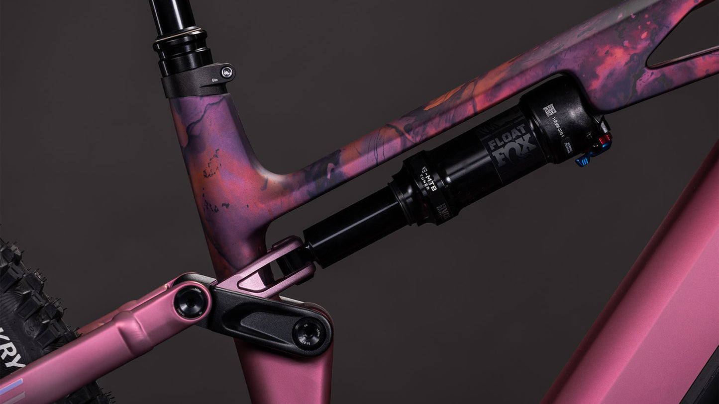 Nahaufnahme des CUBE Stereo Hybrid ONE44 HPC SLX 800 shiftblush'n'art 2026 Fahrradrahmens mit marmoriertem rosa und lila Finish, das die hintere Federung und den Stoßdämpfer vor einem dunklen Hintergrund hervorhebt.