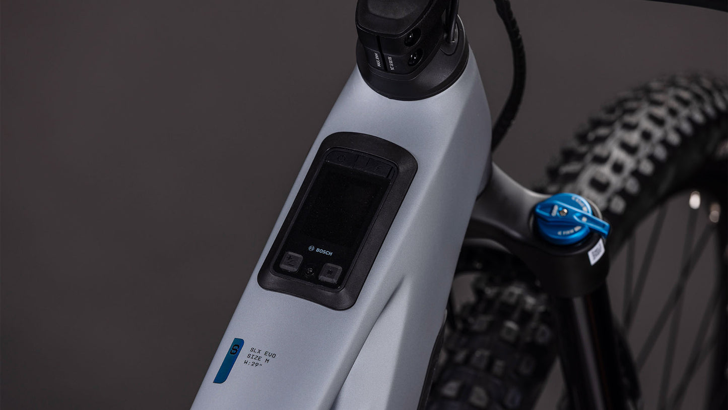 Nahaufnahme des CUBE Stereo Hybrid ONE44 HPC SLX Evo 800 (2026) Rahmens mit einem in das Oberrohr integrierten Bosch-Display. Das slategrey'n'black E-MTB zeigt auch einen Teil des Reifens und der Federgabel vor einem dunklen, unscharfen Hintergrund.