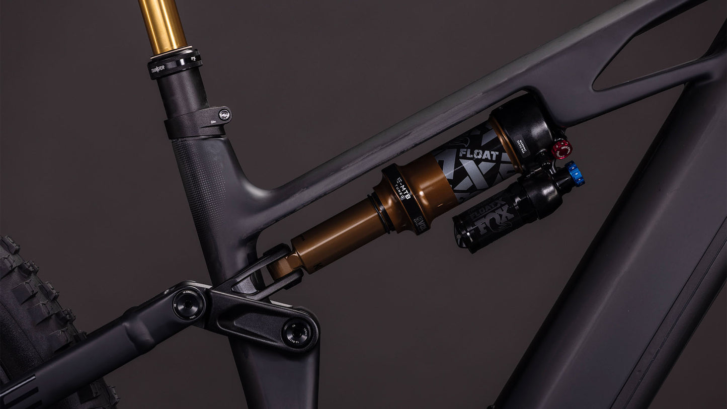 Nahaufnahme des CUBE Stereo Hybrid ONE44 HPC AT 800 carbon'n'gold 2026 Rahmens, der das hintere Federungssystem mit einem FOX Float X Dämpfer auf seiner mattschwarzen Carbonstruktur hervorhebt.