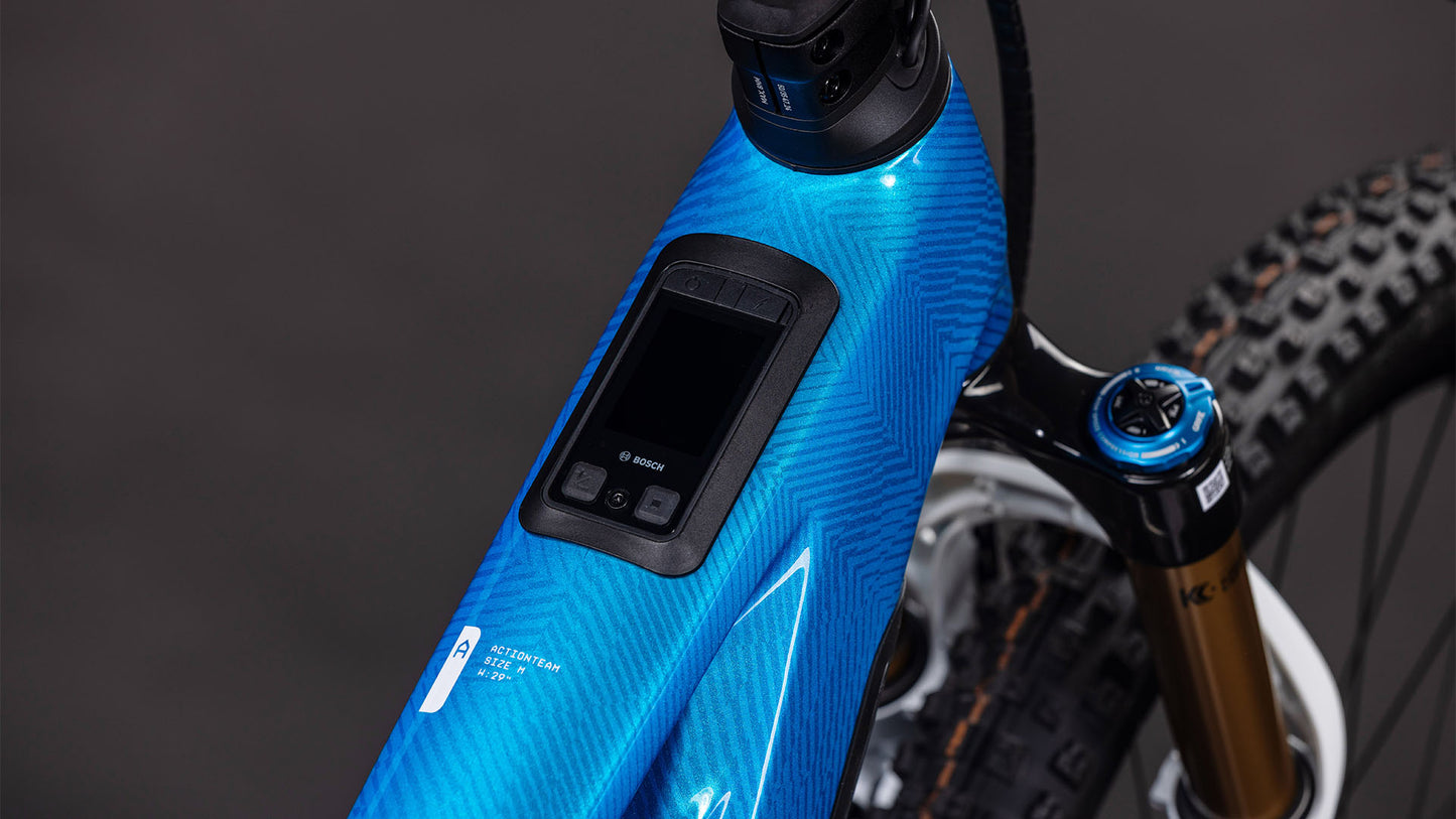 Nahaufnahme des blauen CUBE Stereo Hybrid ONE44 HPC AT 800 actionteam 2026 Rahmens mit integriertem Bosch Display am Oberrohr und leistungsstarkem Bosch CX Motor. Auch ein Teil der vorderen Federgabel und des Reifens ist zu sehen.