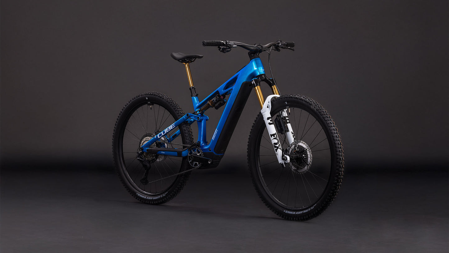 Ein blaues CUBE Stereo Hybrid ONE44 HPC AT 800 actionteam 2026 vollgefedertes Mountainbike mit schwarzen Laufrädern, weißer Vorderradgabel, großer Bereifung, Shimano XT Scheibenbremsen und einem leistungsstarken Bosch CX Motor steht vor einem dunklen Hintergrund.