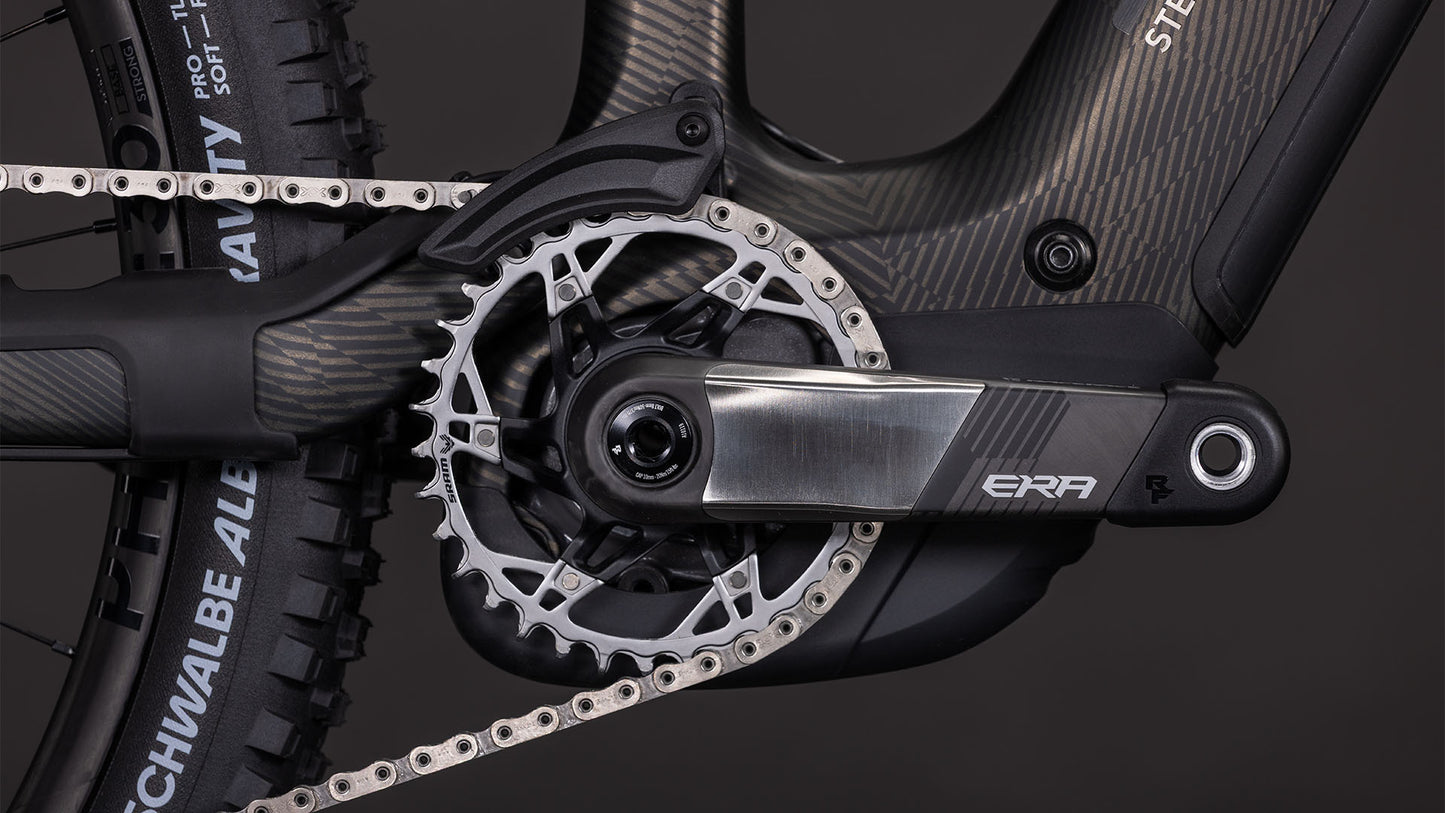 Nahaufnahme der CUBE Stereo Hybrid ONE44 HPC SLT 800 Kurbelgarnitur und des Kettenblatts mit Metallic-Finish, ERA-Logo, All-Mountain-E-Bike-Rahmen, Hinterradreifen, einem Teil der Kette und einem Bosch CX-R Motor. Marke: CUBE.