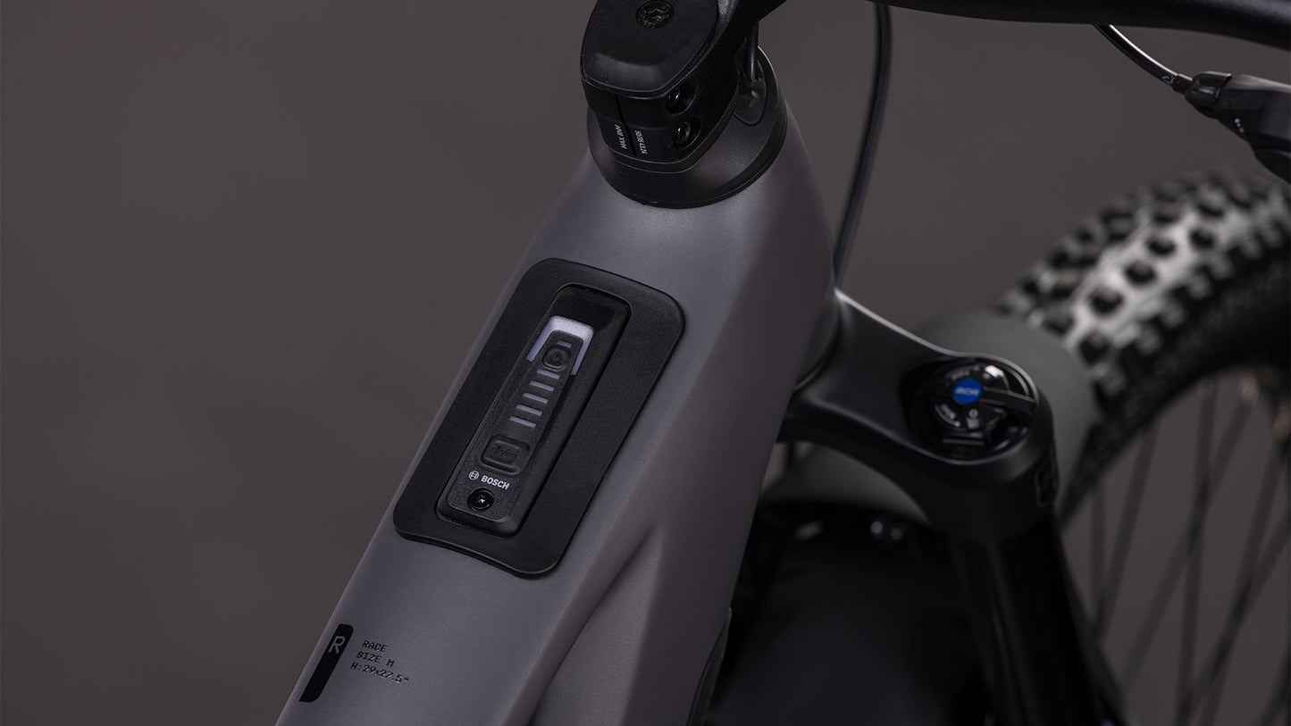 Nahaufnahme des mattgrauen Oberrohrs des CUBE Stereo Hybrid ONE77 HPC Race 800 irongrey'n'black 2026 mit eingebautem Bosch-Bedienfeld und Power-Knopf neben Lenker und Gabel, angetrieben von einem Bosch CX-Motor.