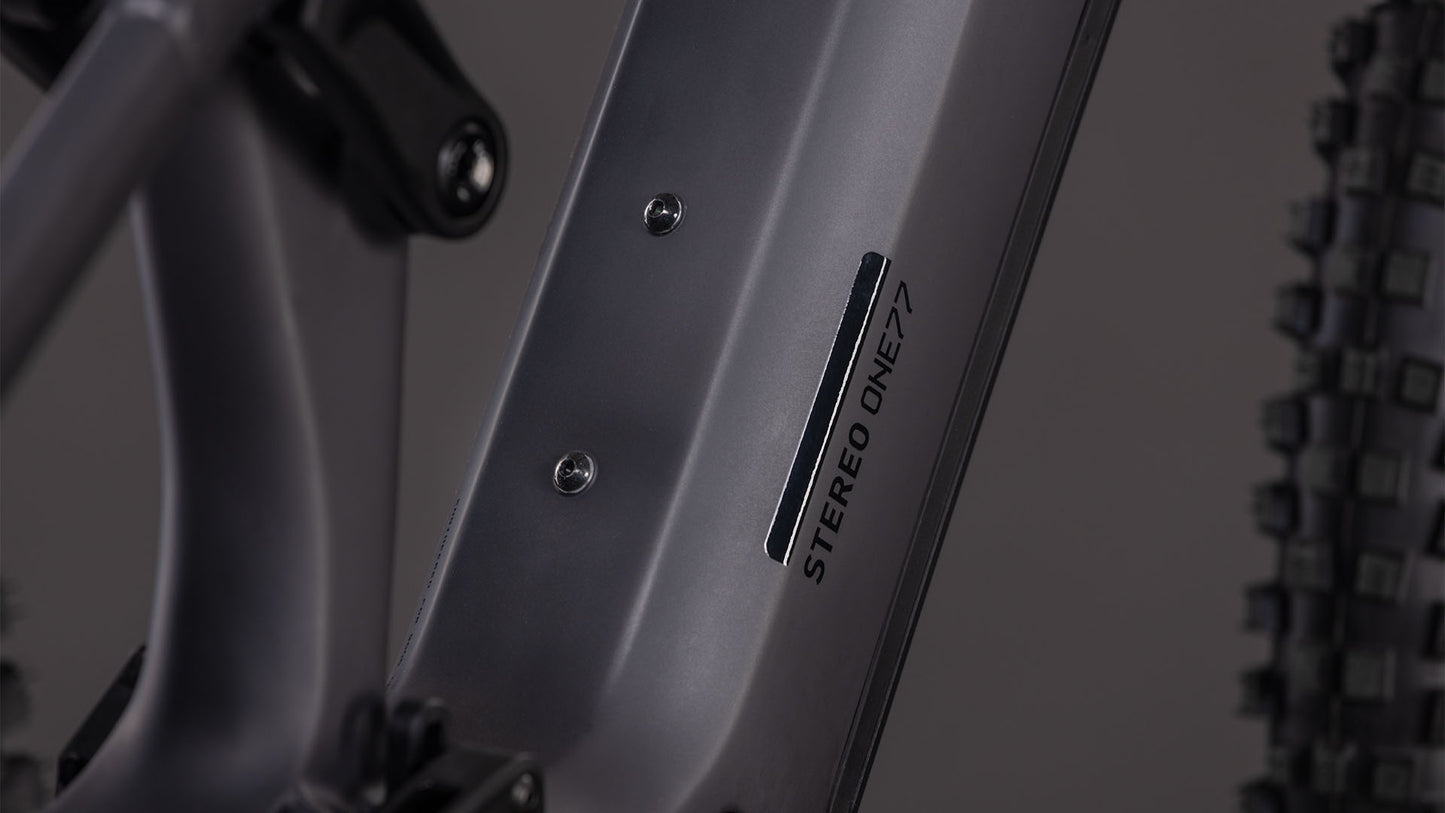 Nahaufnahme des CUBE Stereo Hybrid ONE77 HPC Race 800 in irongrey'n'black, mit dem STEREO ONE77-Logo auf dem Unterrohr, Hinterradfederung, Noppenreifen und Shimano XT 12-fach Schaltung im Hintergrund.