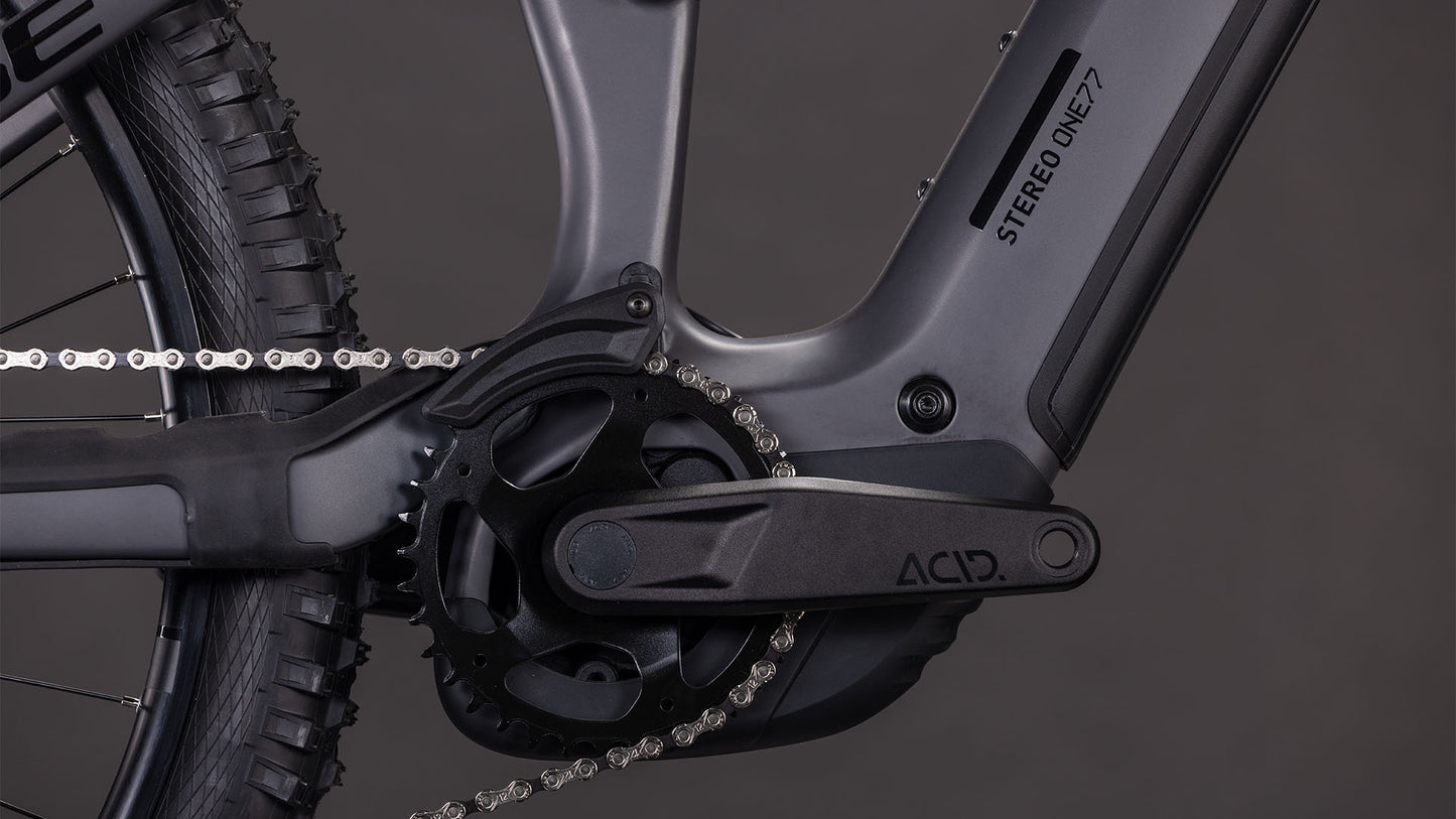 Nahaufnahme einer schwarzen Kurbelgarnitur, Kette und Rahmen des CUBE Stereo Hybrid ONE77 HPC Race 800 irongrey'n'black 2026, mit sichtbarer STEREO ONE77. Der dunkle Hintergrund hebt das Design und die Details der Shimano XT 12-fach Schaltung hervor.