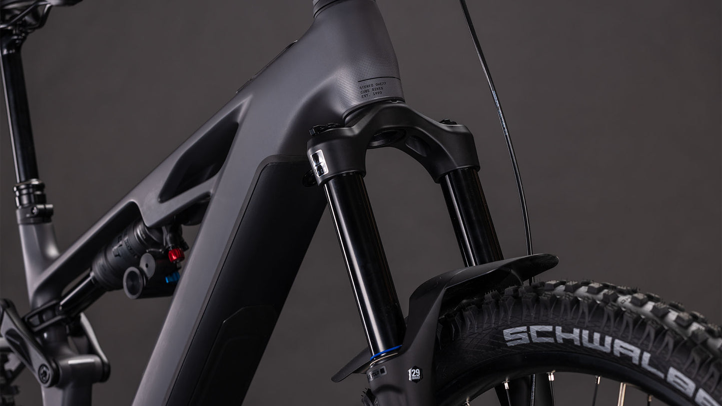 Nahaufnahme des CUBE Stereo Hybrid ONE77 HPC Race 800 Mountainbikes in irongrey'n'black (2026), die die robuste Federgabel, den dicken Rahmen und den Schwalbe-Vorderreifen vor einem dunklen Hintergrund hervorhebt.