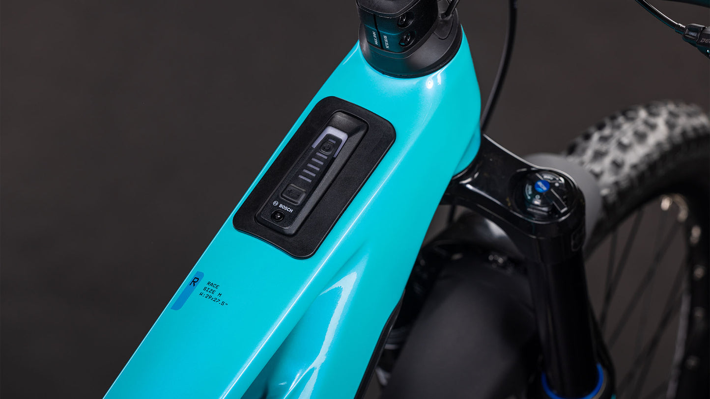 Nahaufnahme des Oberrohrs des CUBE Stereo Hybrid ONE77 HPC Race 800 swimmingpool'n'black 2026. Zu sehen sind das integrierte Bosch-Display, das Bedienfeld, ein Teil der Federgabel, ein Noppenreifen und die Shimano XT 12-Gang-Schaltung.