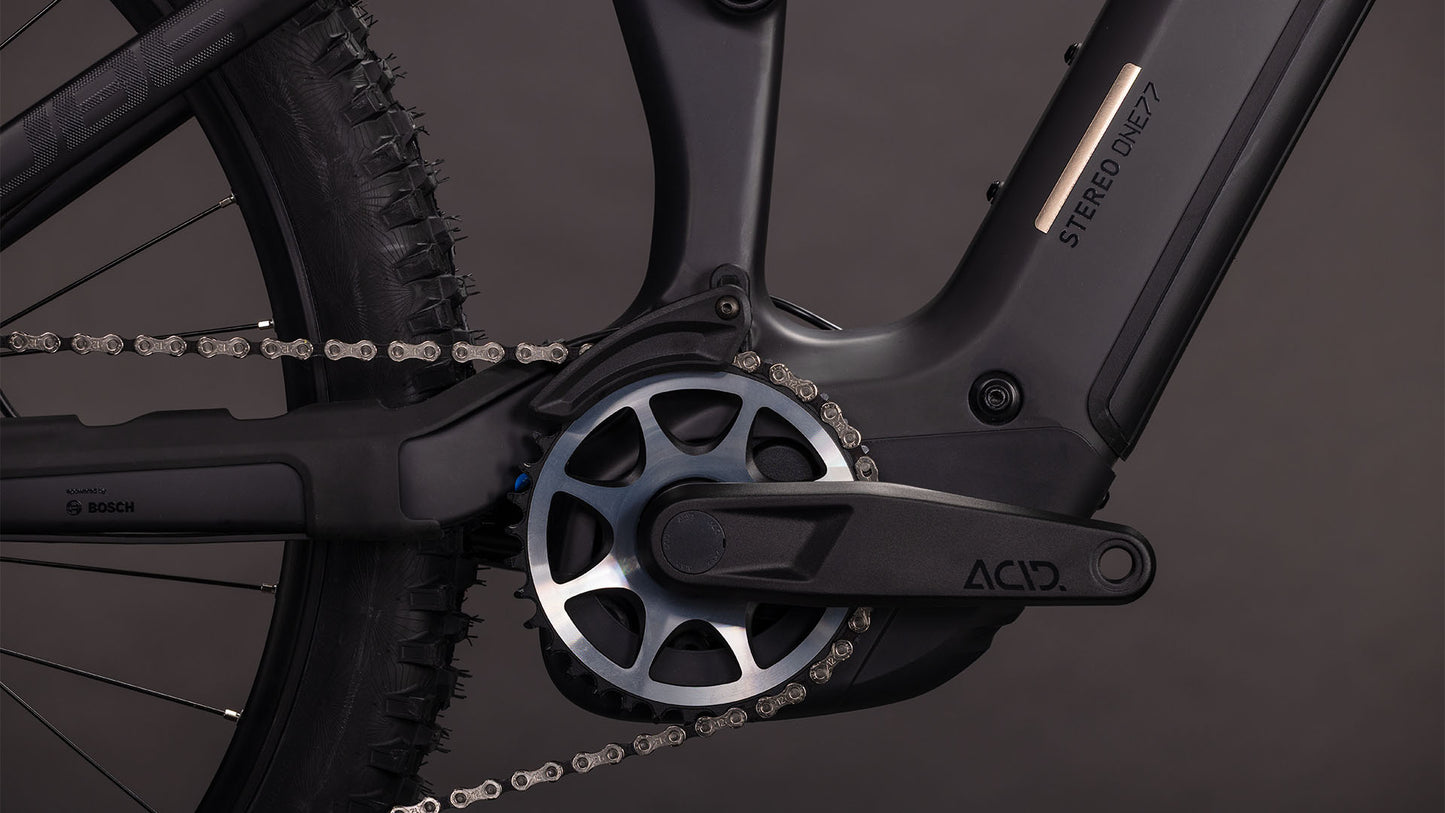 Nahaufnahme der Kurbelgarnitur, der Kette, des Pedals, des vorderen Ritzels und des Bosch CX Motors am CUBE Stereo Hybrid ONE77 HPC SLX 800 blackline 2026. Der Rahmen ist mit Stereo ONE77 170 mm Federweg gekennzeichnet. Dunkler, minimaler Hintergrund.