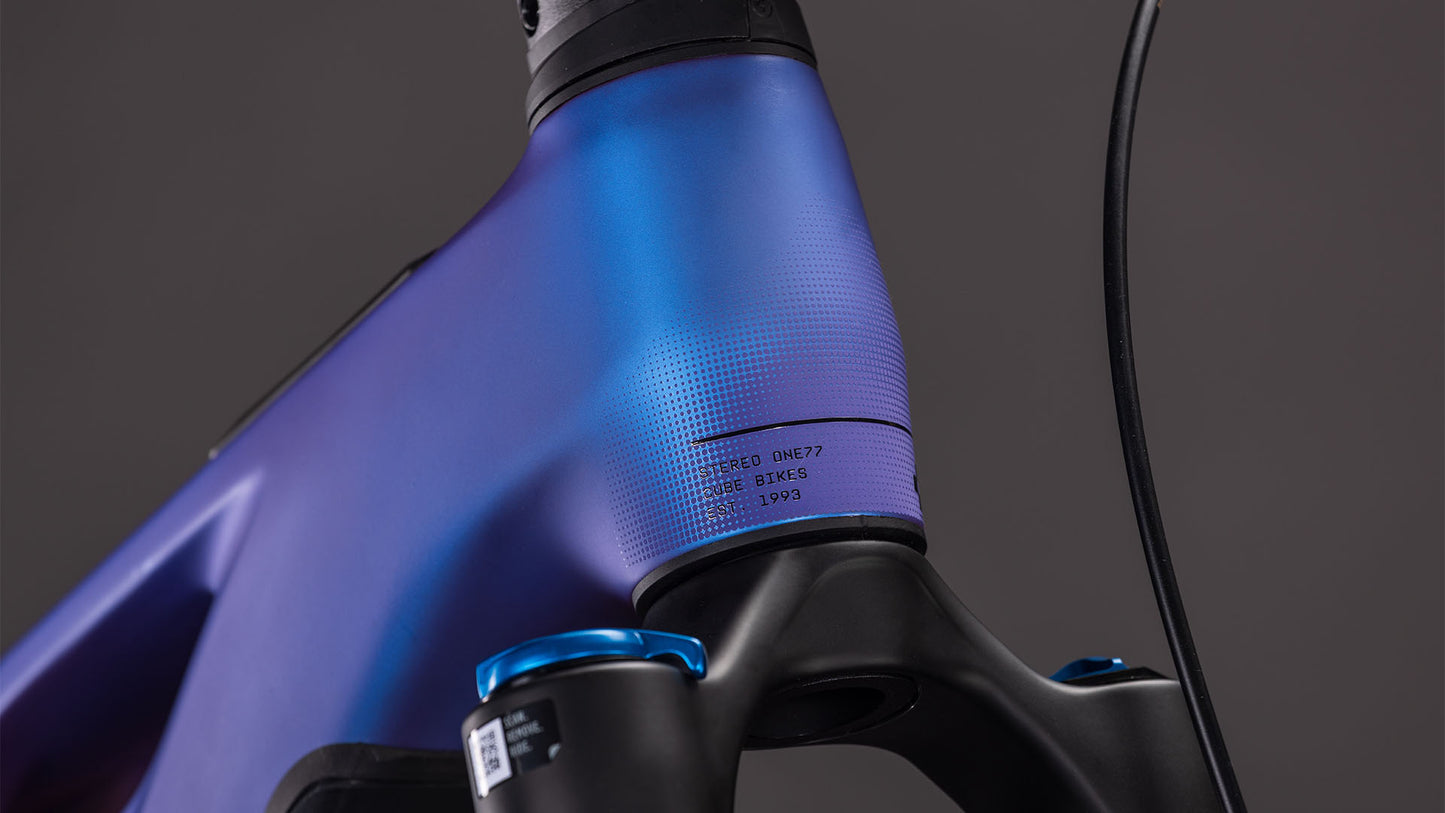 Nahaufnahme des CUBE Stereo Hybrid ONE77 HPC SLX 800 in blueiris'n'black (2026). Hervorzuheben sind der blau-violette Rahmen mit Farbverlauf, die 170-mm-Federgabel, das schwarze Kabel und die kleine Modellnummer am Steuerrohr.