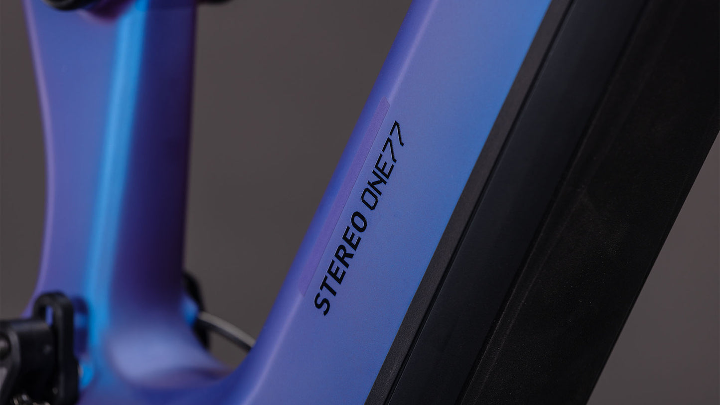 Nahaufnahme eines CUBE Stereo Hybrid ONE77 HPC SLX 800 blueiris'n'black 2026 Rahmens mit sanftem blau-violettem Farbverlauf und STEREO ONE77 in schwarzer Schrift auf dem schrägen Rohr; der Hintergrund ist unscharf.