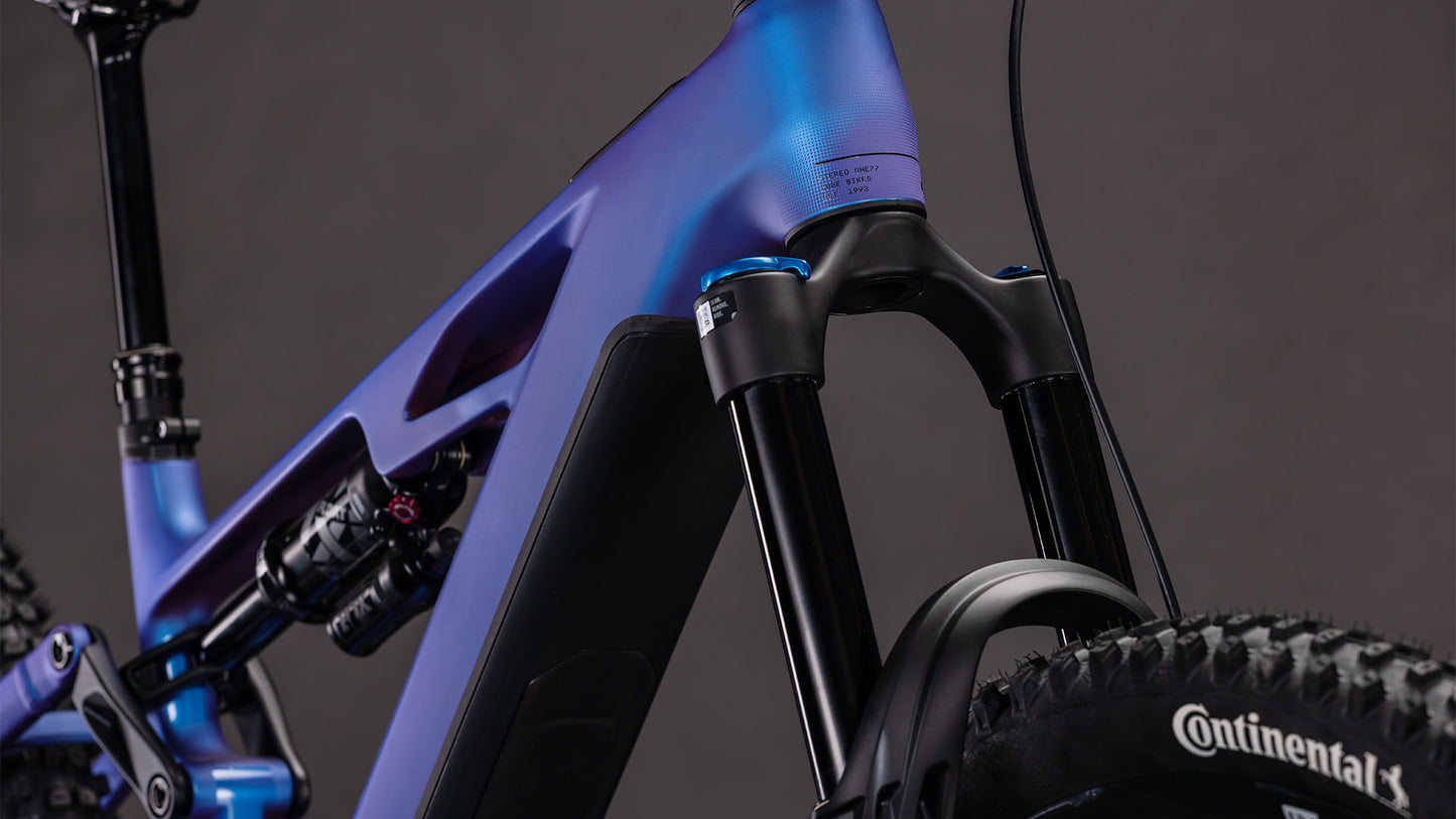 Nahaufnahme des CUBE Stereo Hybrid ONE77 HPC SLX 800 blueiris'n'black 2026 E-MTB, mit Bosch CX-Motor, Federgabel vorne, mattblauem Rahmen, Stoßdämpfer hinten und Continental-Reifen vor dunklem Hintergrund.