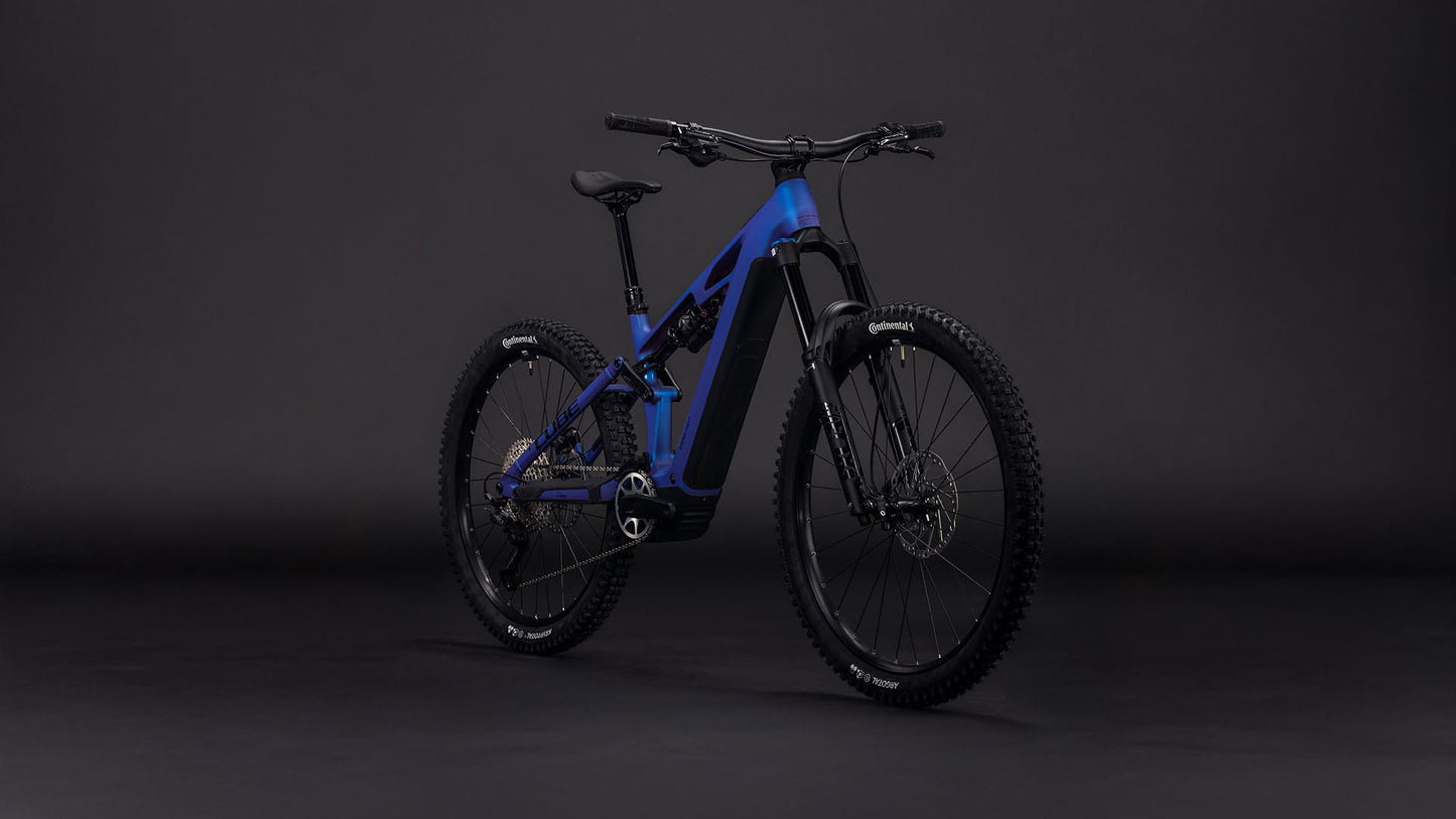 Das CUBE Stereo Hybrid ONE77 HPC SLX 800 in blueiris'n'black 2026 ist mit dicken Off-Road-Reifen, einem robusten Rahmen, einer fortschrittlichen Federung und einem Bosch CX-Motor vor einem dunklen, minimalistischen Hintergrund ausgestattet - ideal für raues Terrain.