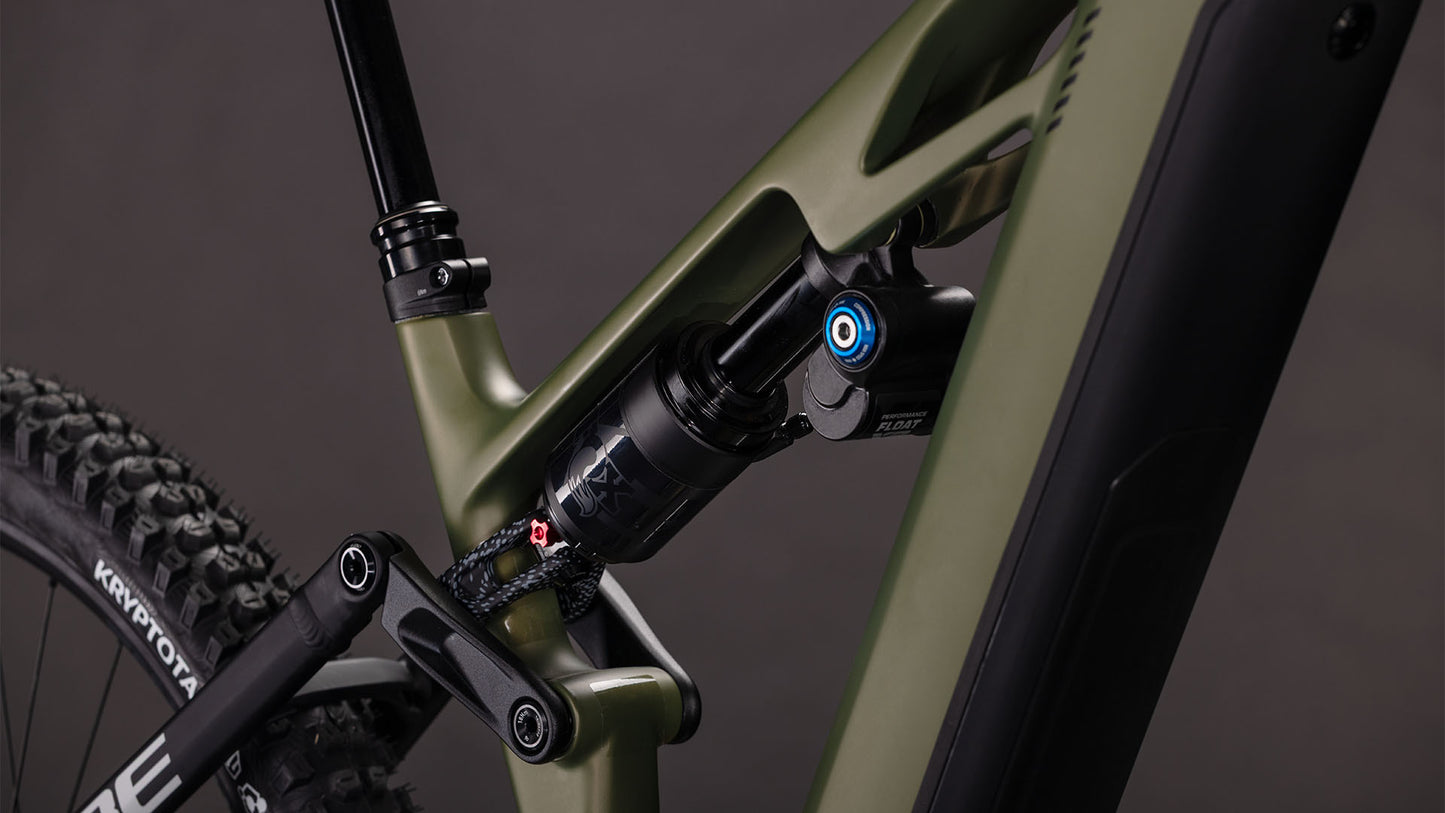 Nahaufnahme des CUBE Stereo Hybrid ONE77 HPC TM 800 reedgreen'n'matrix 2026, die den mattgrünen Rahmen, das Federbein, die schwarzen Komponenten und einen Teil des Hinterrads vor einem dunklen Hintergrund zeigt.